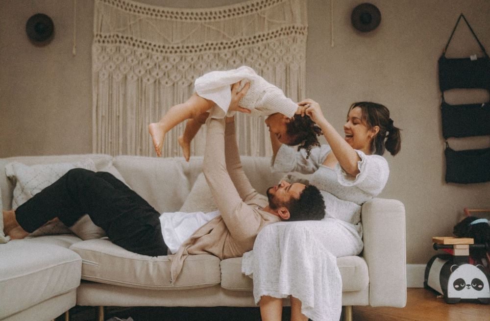 Mum & dad playing with child on a sofa. Family documentary photography