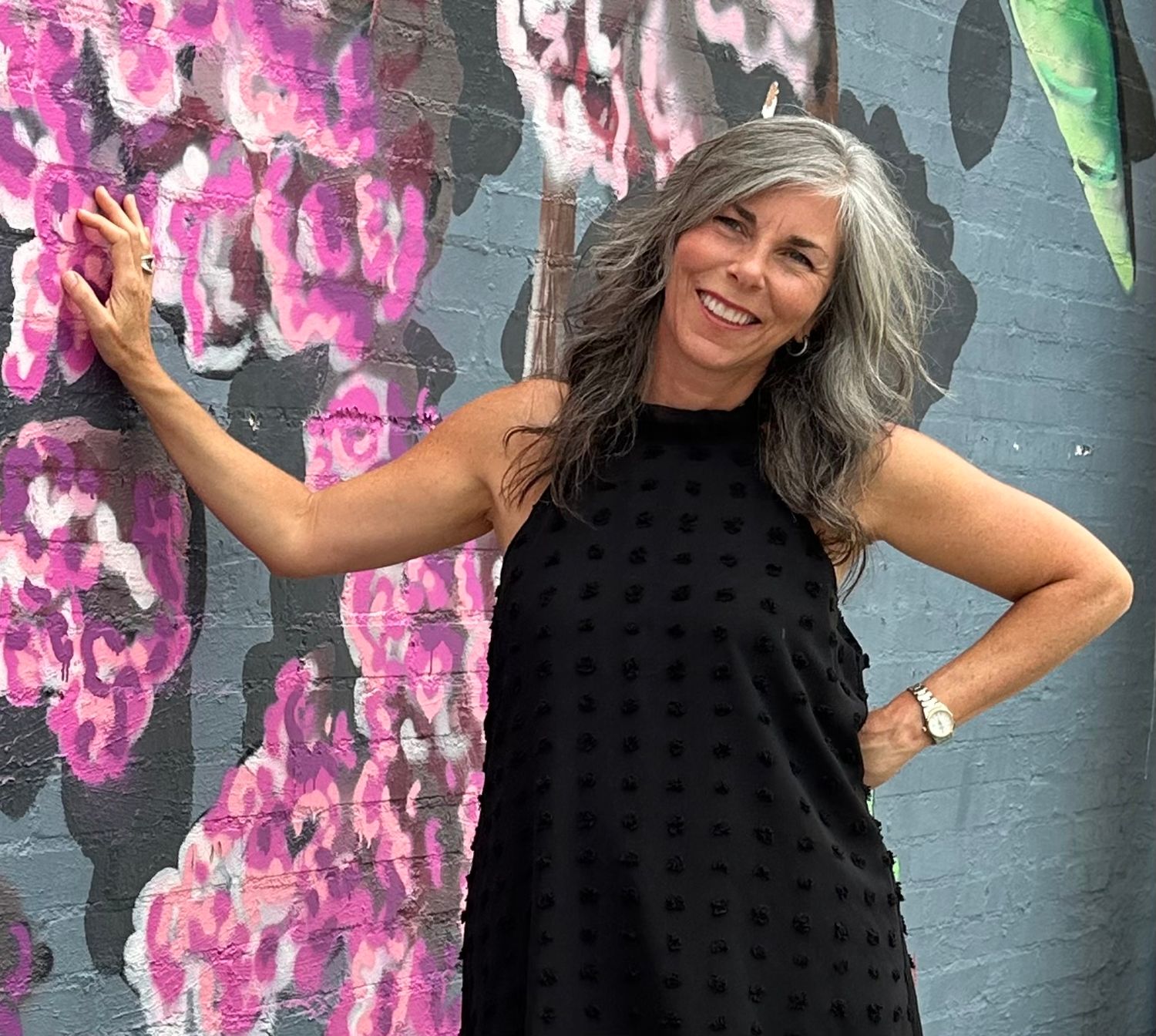 Evalina Huckaby is the owner of Sanctuaire Atelier Venue. She is a woman leaning against a floral graffiti wall.