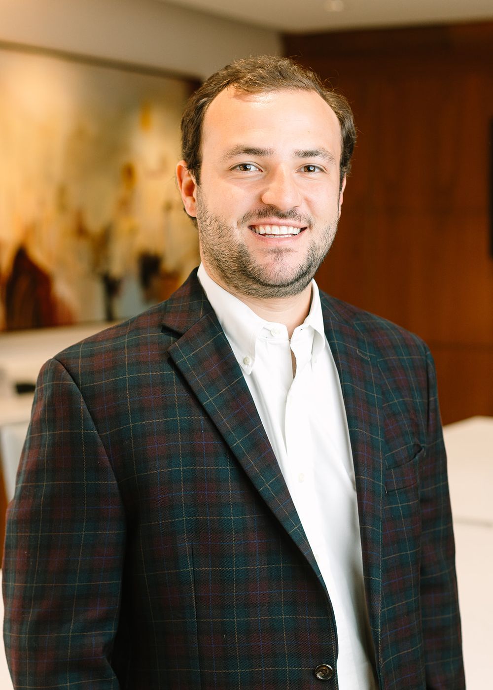 A professional headshot of someone wearing a white dress shirt and green plaid sport coat with a smile.