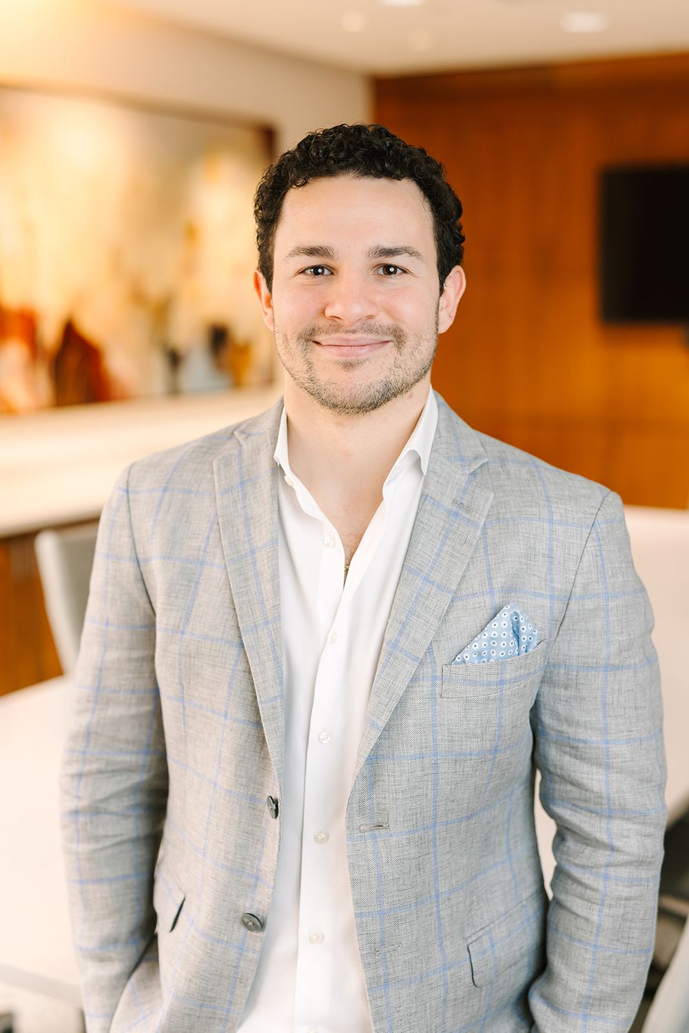 Professional headshot of someone in a light gray windowpane blazer and white shirt with a light blue pocket square.