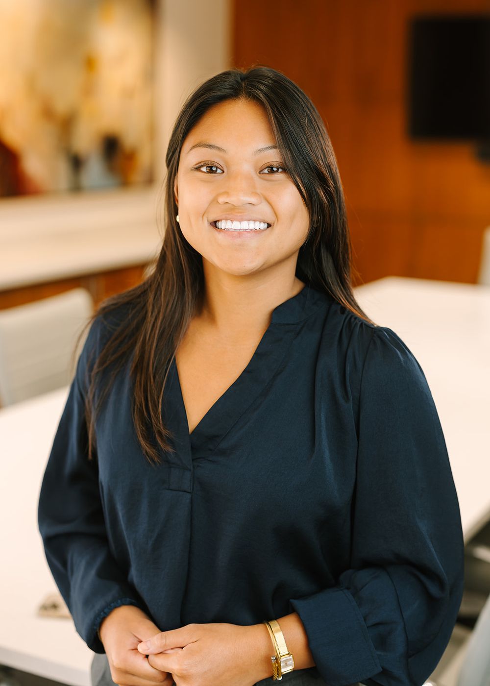 Professional portrait of someone in a navy blue blouse smiling warmly against a light interior background.