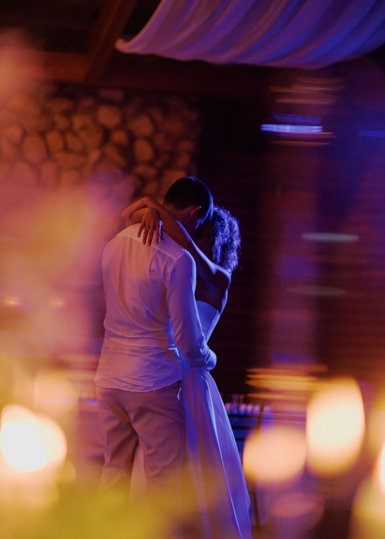 Bride and groom share an intimate slow dance bathed in purple and golden reception lighting.