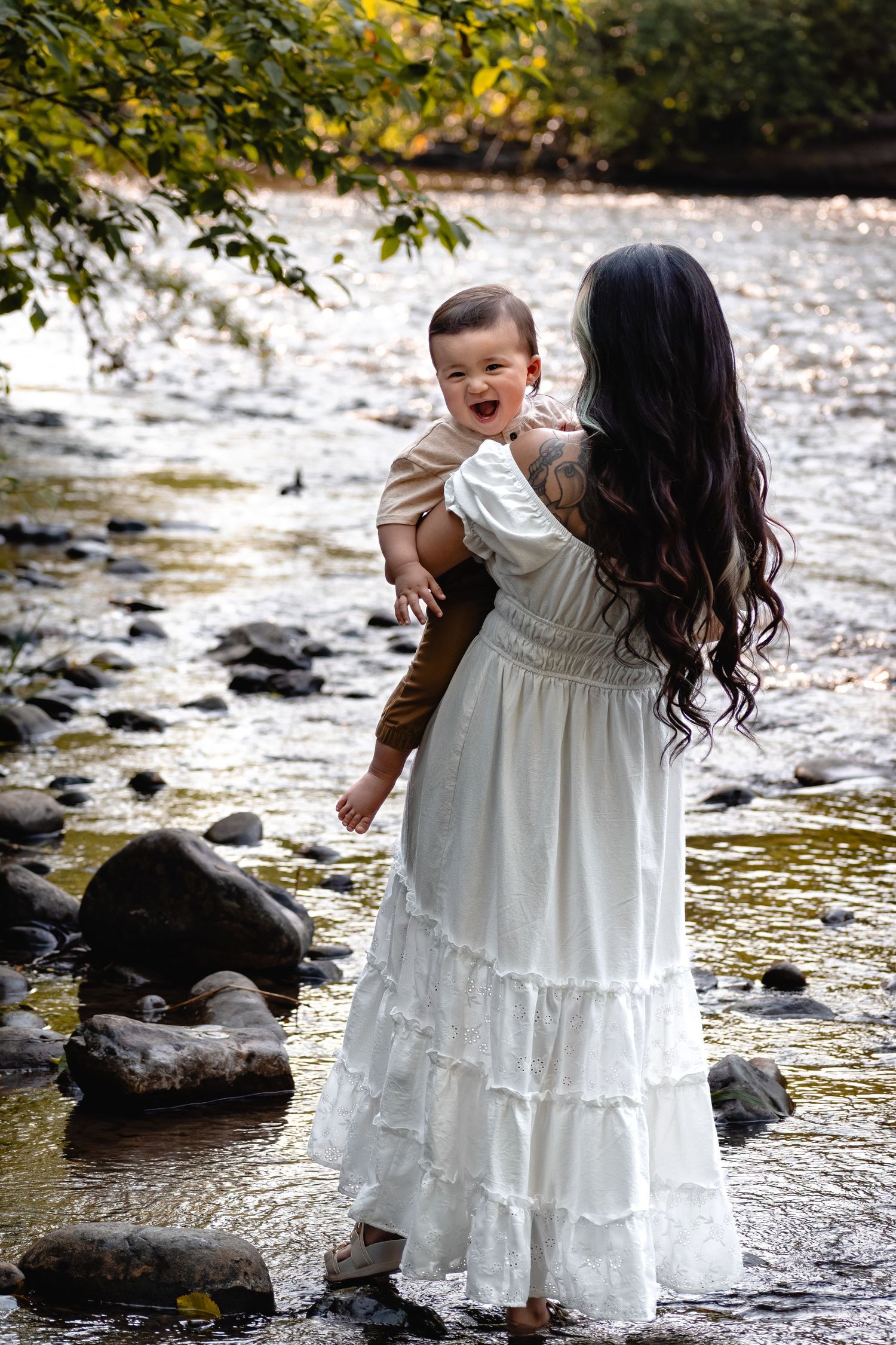 Mother holding smiling one-year-old son by the river during golden hour photos at Flaming Geyser State Park in Washington