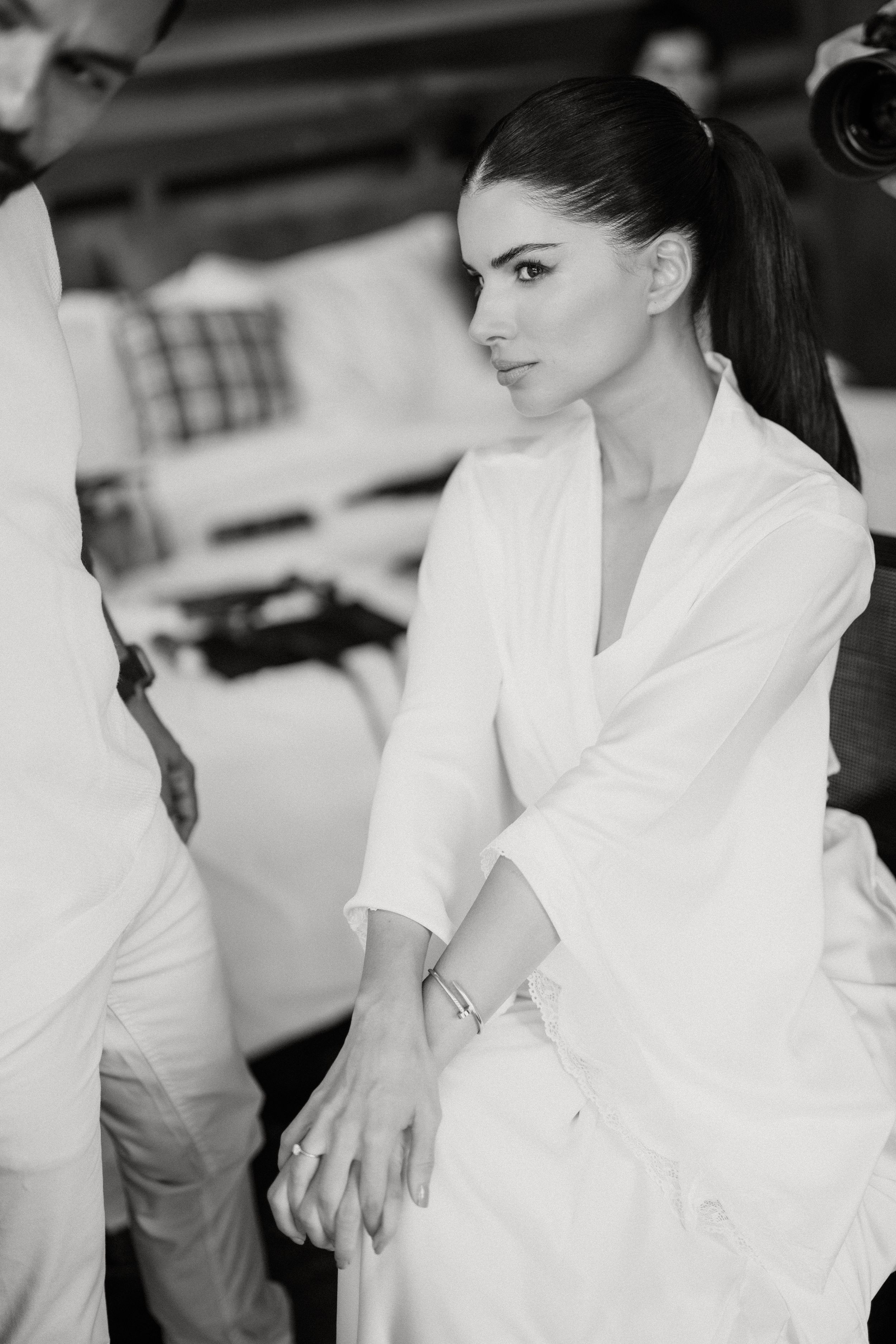 Black and white profile shot showing a figure in a crisp white robe, with dark hair tied back in a sleek ponytail.