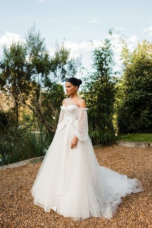 Elegant off-shoulder wedding gown with lace bell sleeves and flowing tulle skirt photographed in outdoor garden setting.