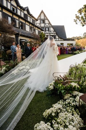Long flowing white cathedral veil with lace trim blowing in the wind against a Tudor-style venue with blooming white flowers.