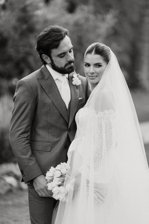 Black and white wedding portrait of bride in white veil and groom in grey suit sharing an intimate moment outdoors.