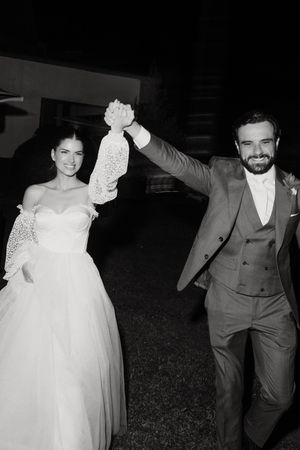 A joyful black and white wedding photo showing newlyweds celebrating with raised hands at an outdoor evening reception.