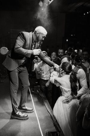 A performer in a suit interacts energetically with audience members from a stage during a black and white concert photo.