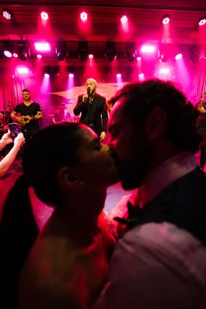 Dance floor crowd illuminated by vibrant pink and red stage lighting at a nightclub party or concert venue.