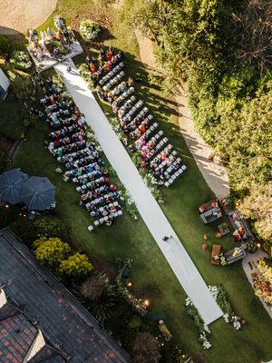 Aerial view of an outdoor wedding ceremony with white aisle runner and rows of chairs on a manicured lawn.