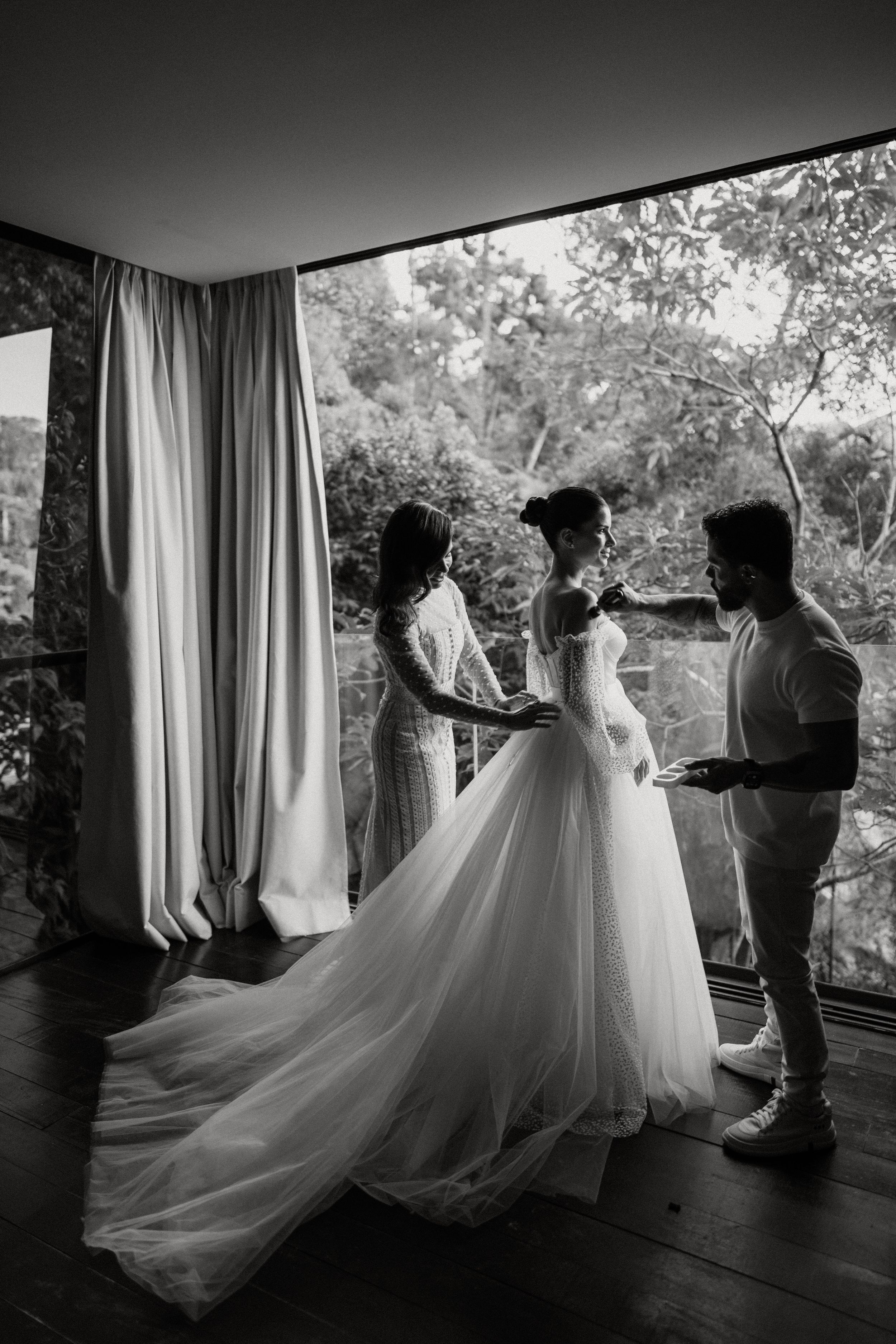 A sequence of black and white silhouettes showing a wedding dress being put on in a sunlit room with flowing curtains.