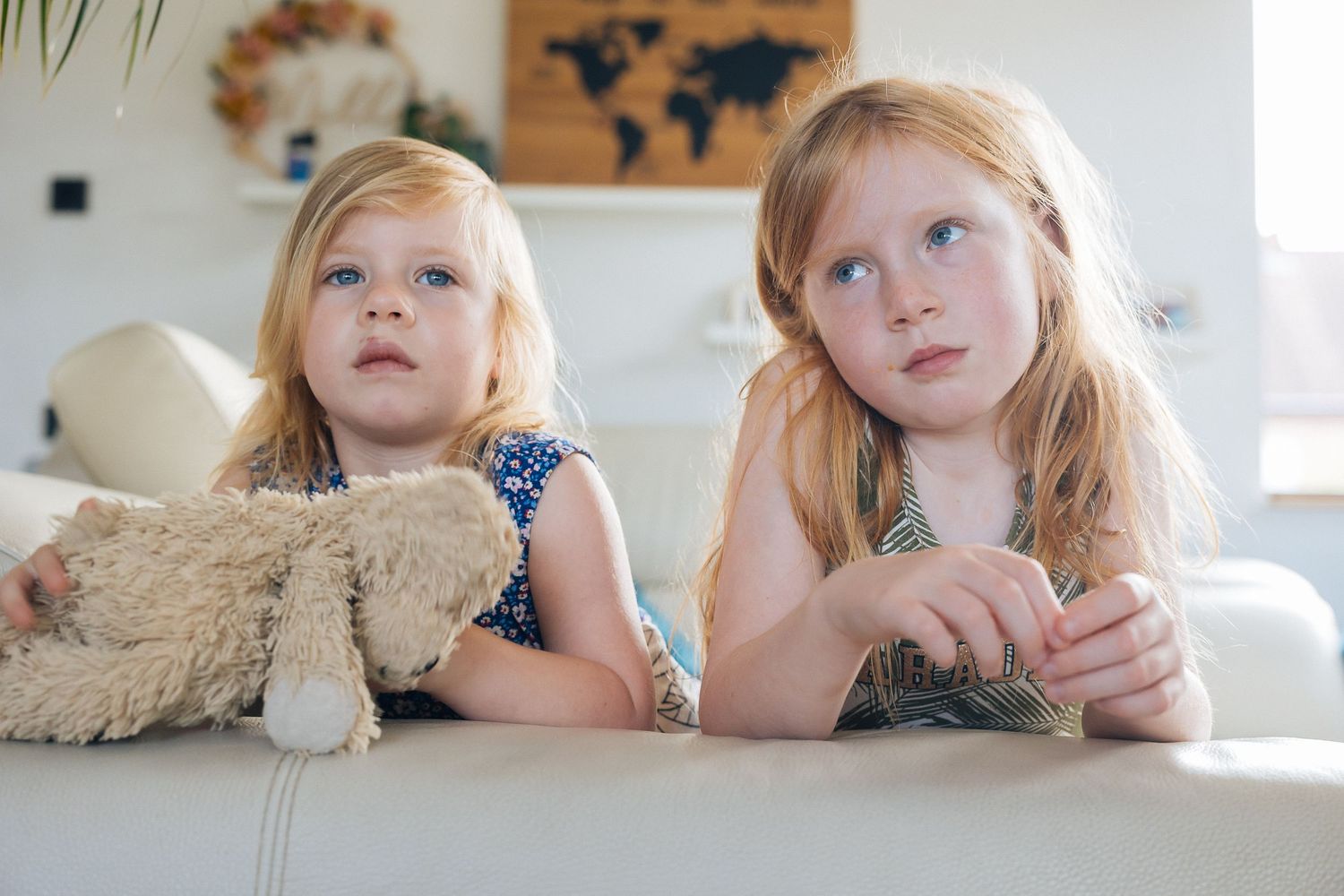 Two children lying on a couch with stuffed animals beneath a world map wall decoration.