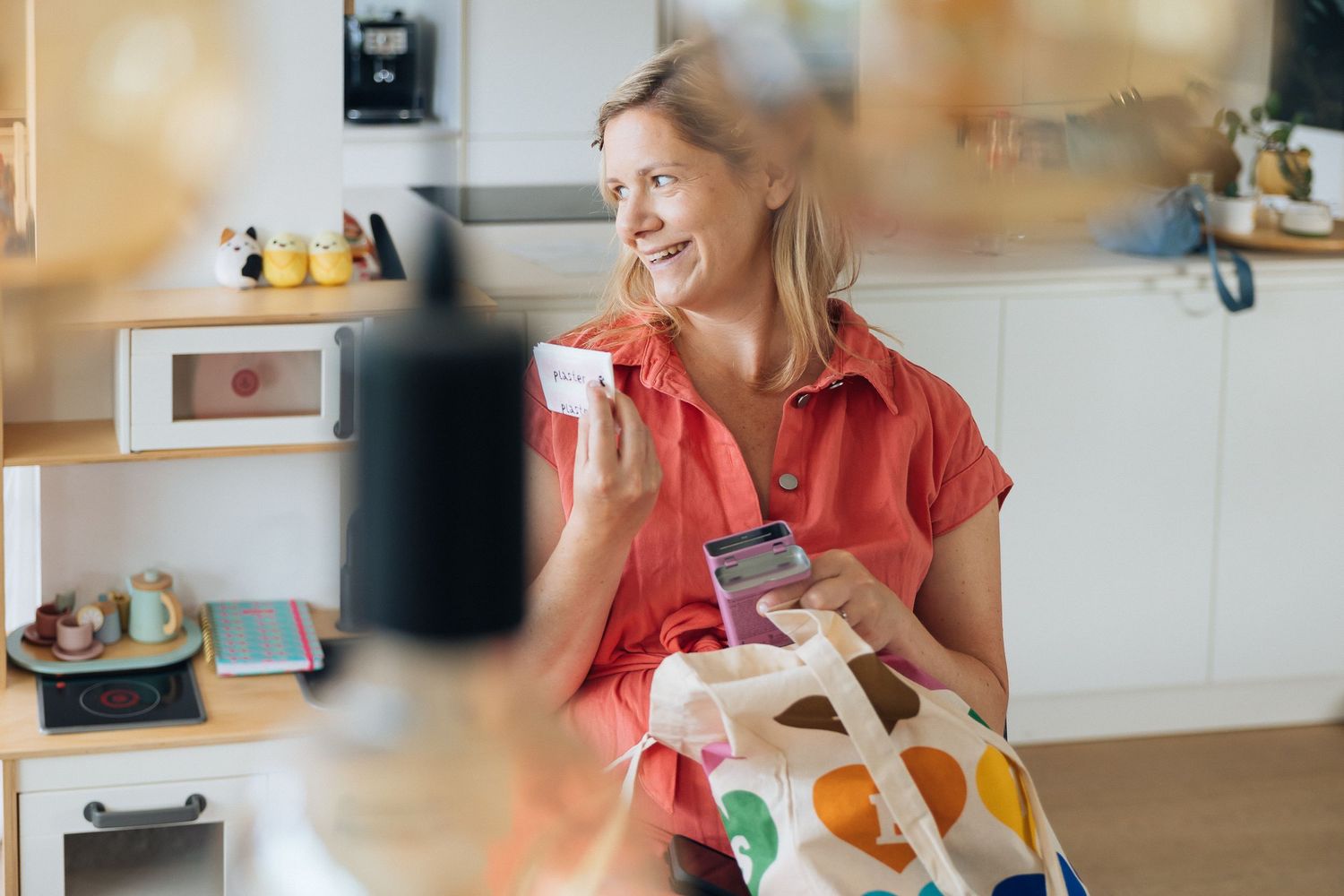 Woman in red shirt sitting in kitchen with colorful shopping bag.