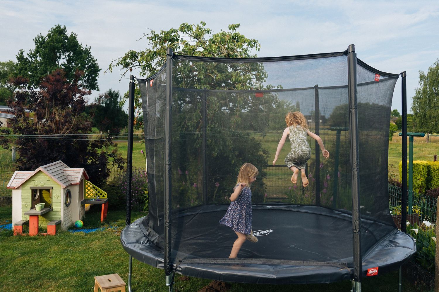 Children jumping and playing on backyard trampoline with safety net.