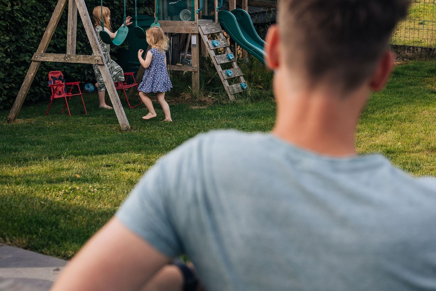 Children playing on backyard playground equipment while being supervised.