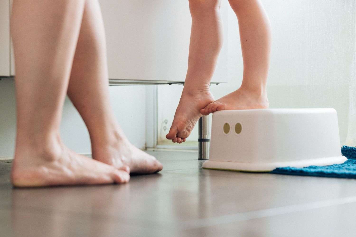 Bare feet reaching for a white step stool on a hardwood floor.