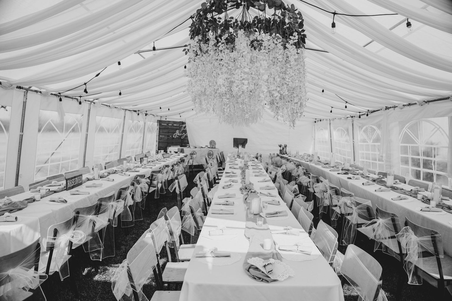 Interior view of an elegant white wedding reception tent with formal table settings and string lights.