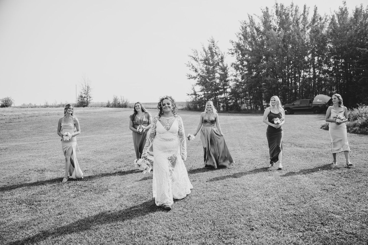 Large wedding group walking through a grassy field during an outdoor celebration.