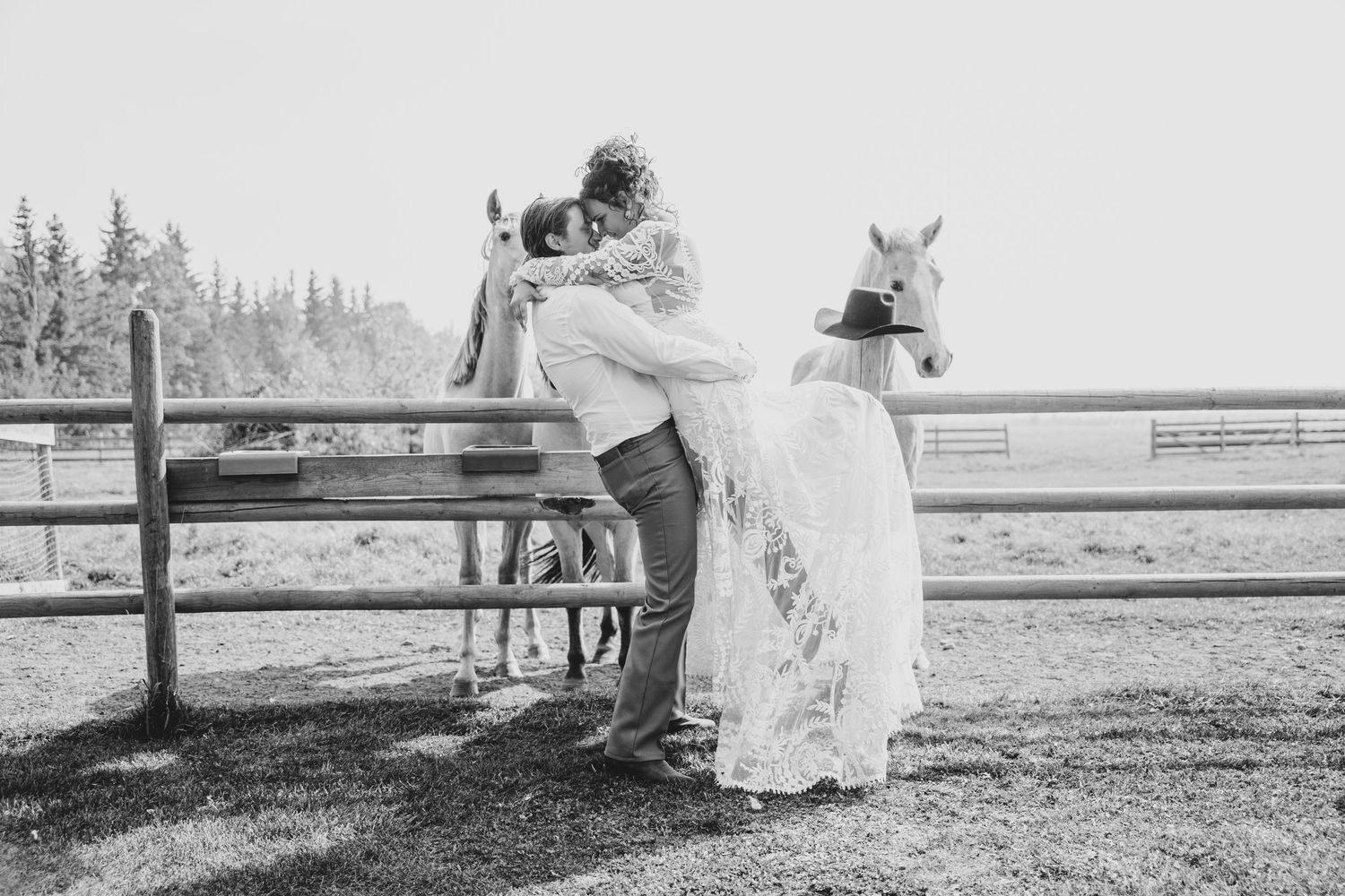 A romantic wedding photo with a couple posing near a horse and wooden fence in black and white.