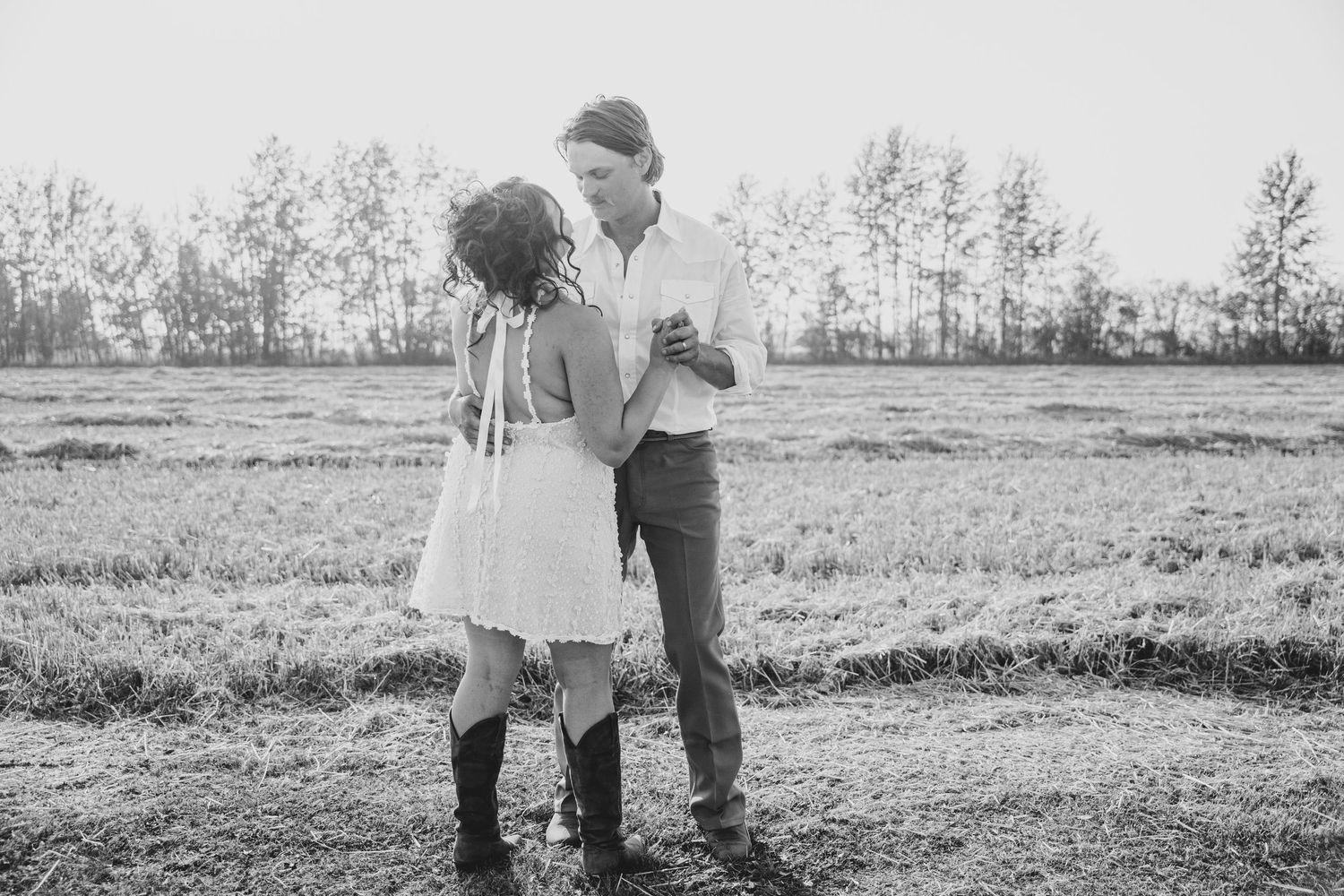 A happy couple walks hand in hand through a sunlit field during their engagement photo session.