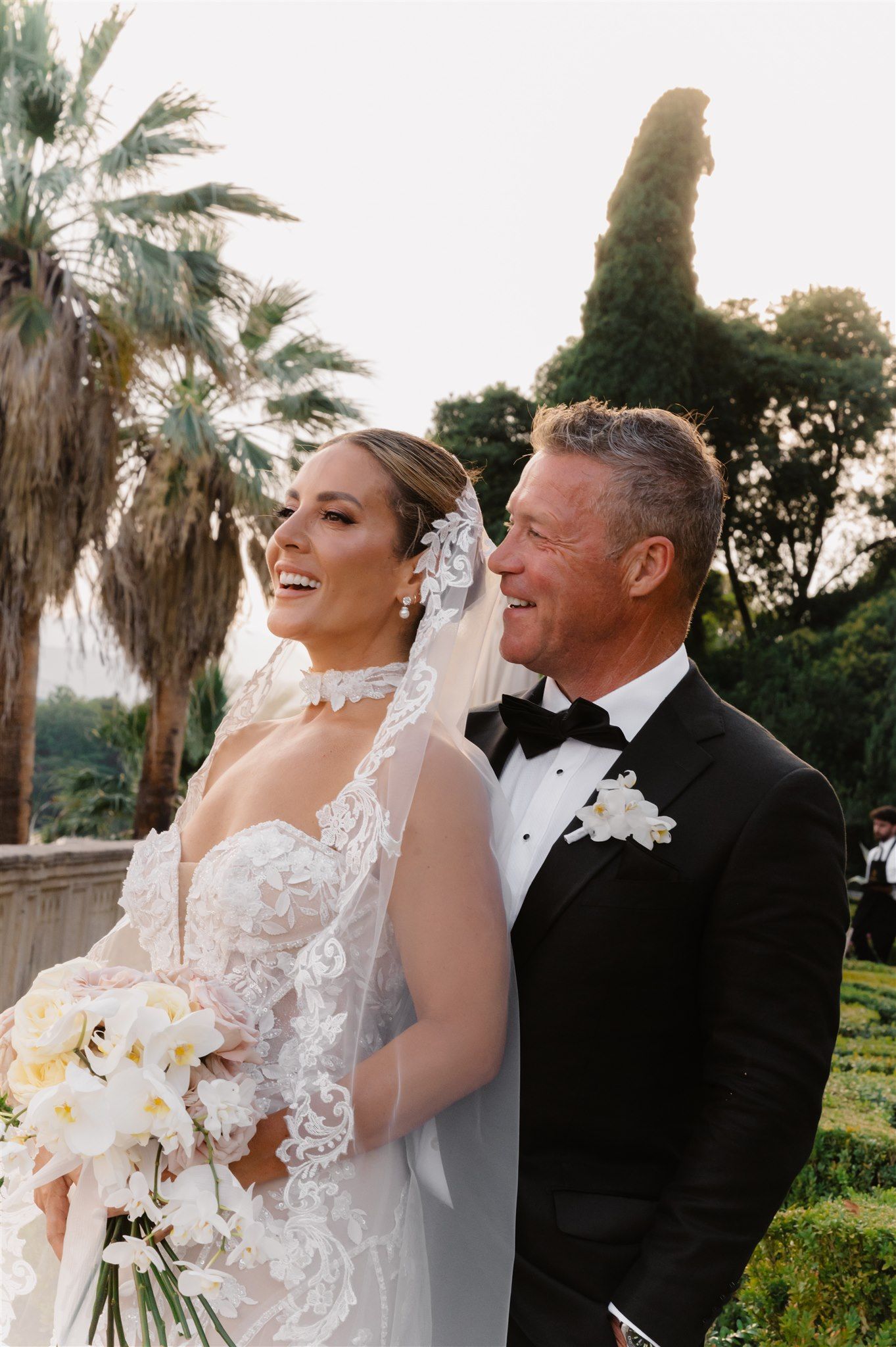 Elegant wedding couple posing among palm trees at sunset.