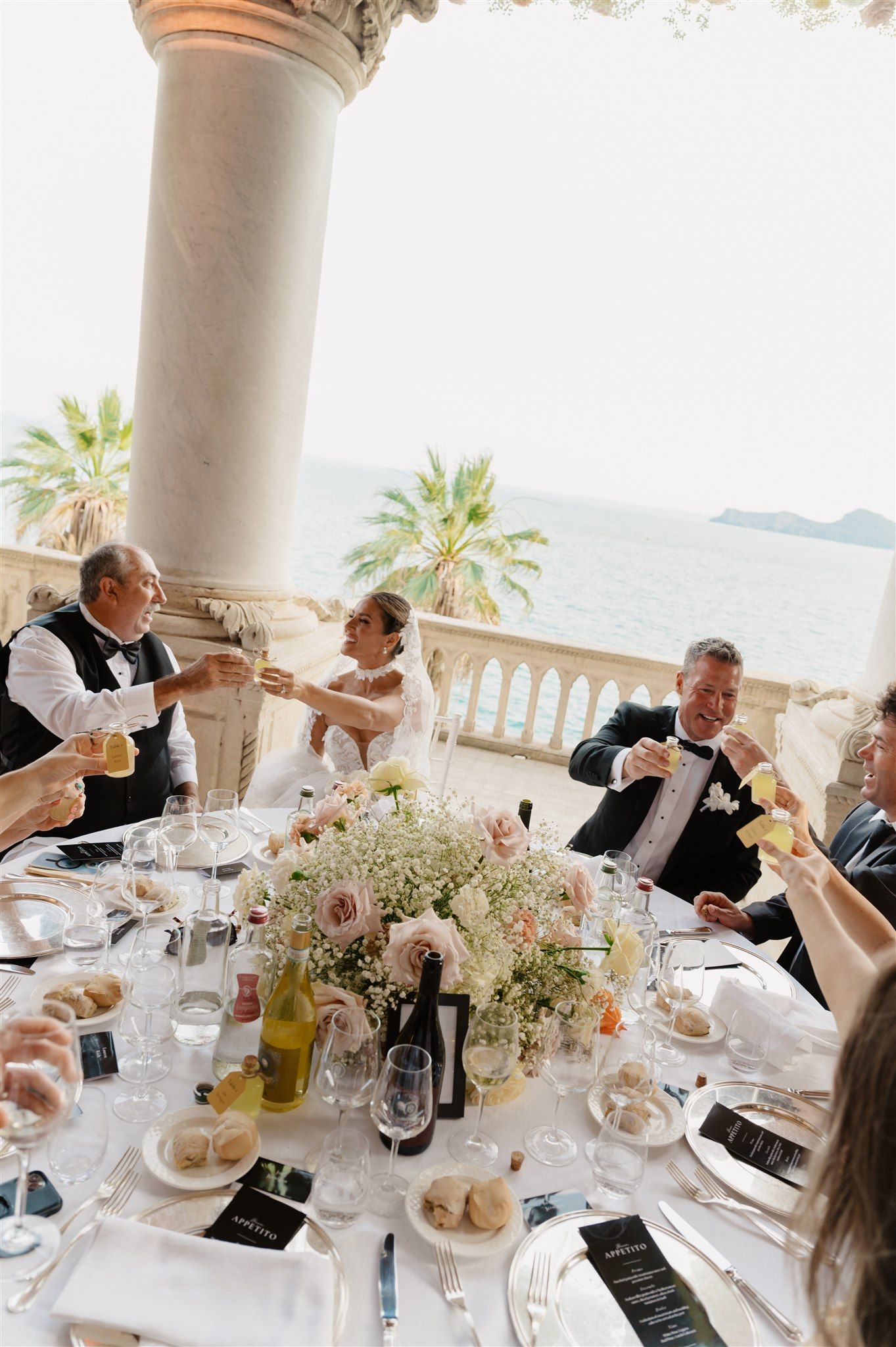 Elegant wedding reception table setting with floral centerpieces and guests dining under ornate columns.