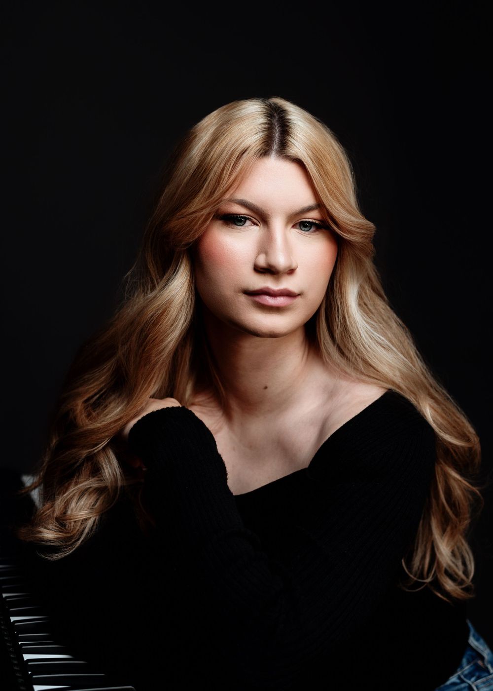 Dramatic portrait of woman in black sweater with long blonde hair against dark background.