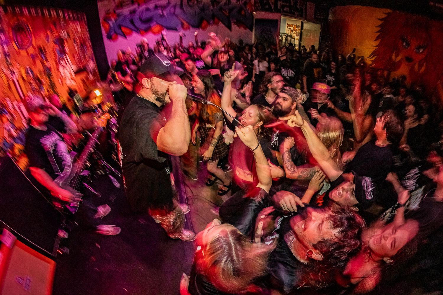 Energetic crowd at a concert venue with red lighting and raised hands.