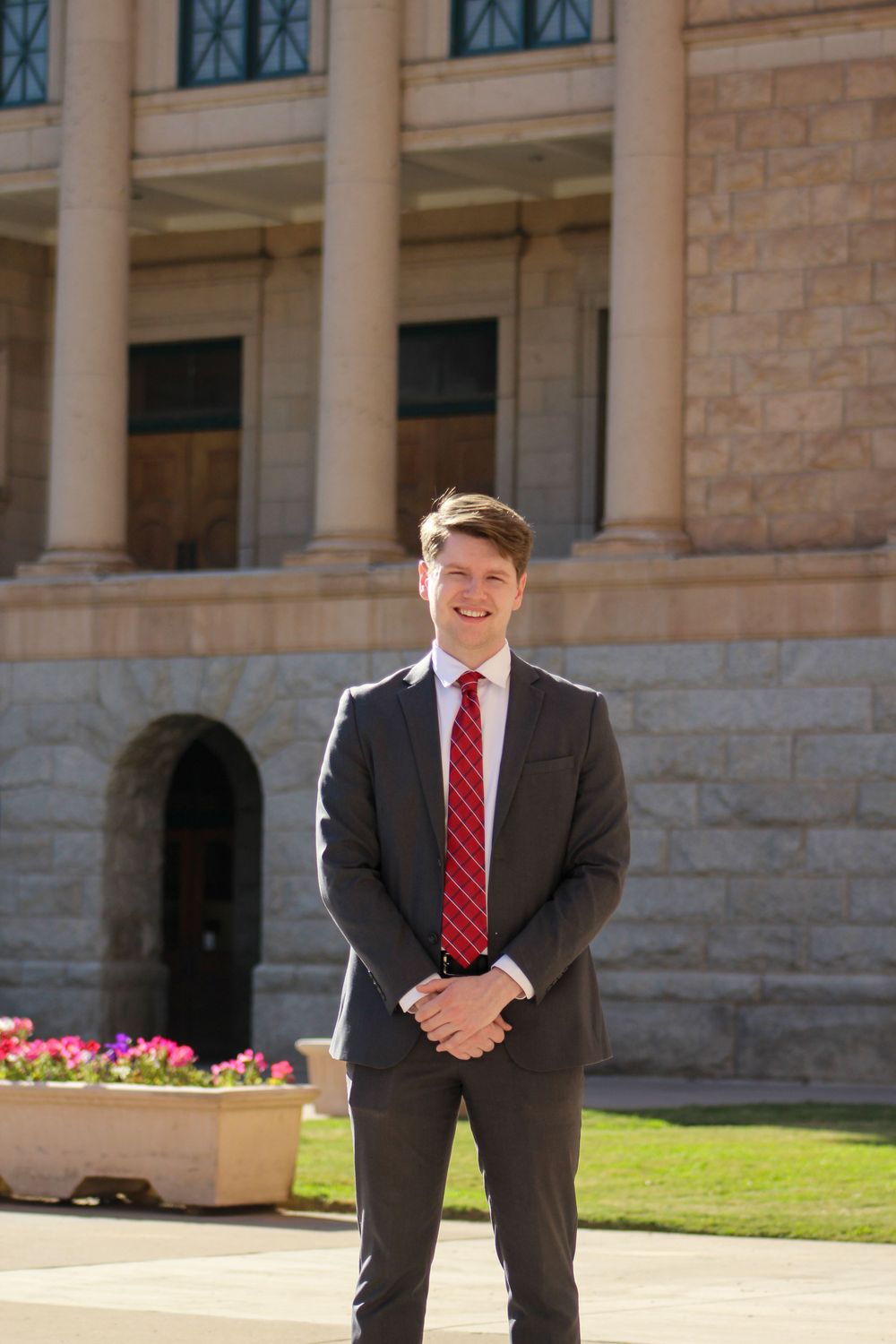 Young professional man in gray suit and red tie standing outside a government building.