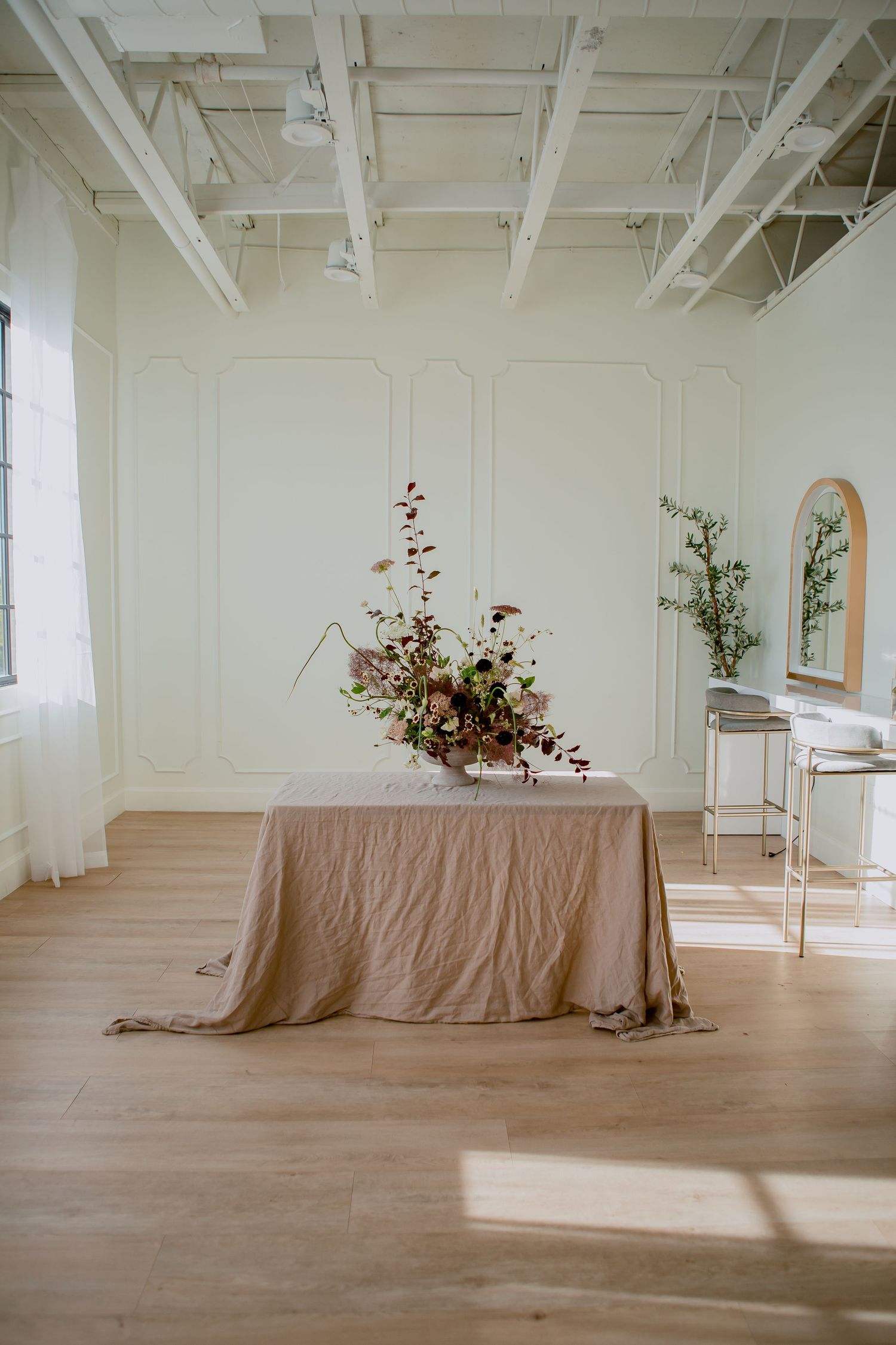 Minimalist studio space with floral arrangement on draped table and white industrial ceiling.