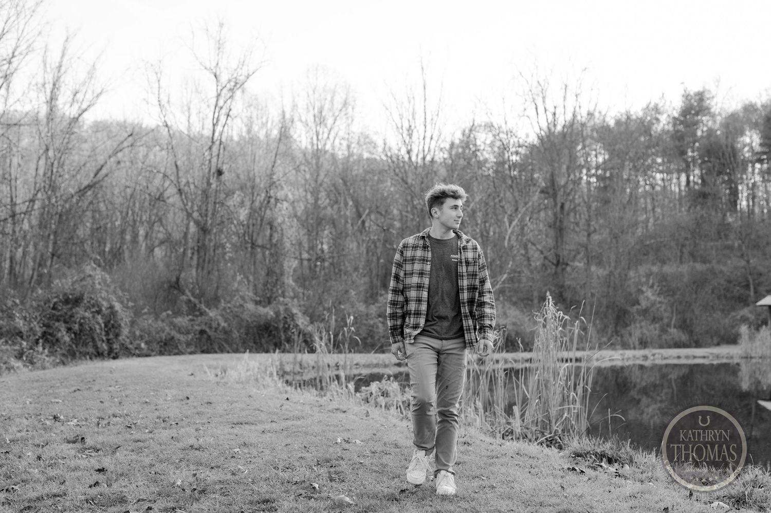 Black and white photo of someone standing on a lakeside path wearing plaid and jeans.