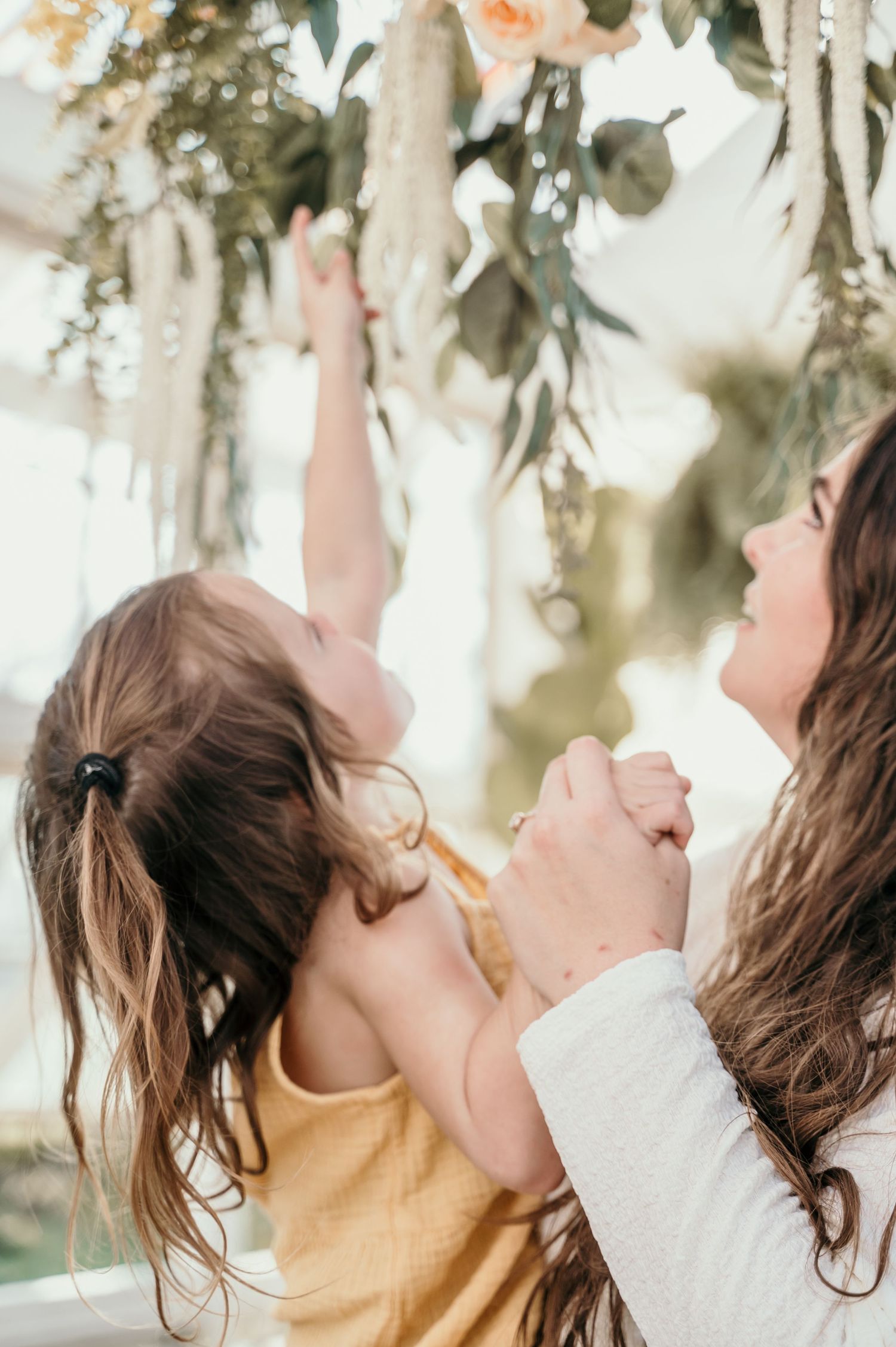 Mother and child reaching up to touch floral decorations together.