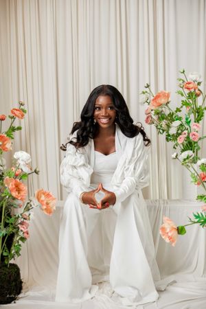 Portrait session with flowing white dress against light curtain backdrop with coral floral arrangements.
