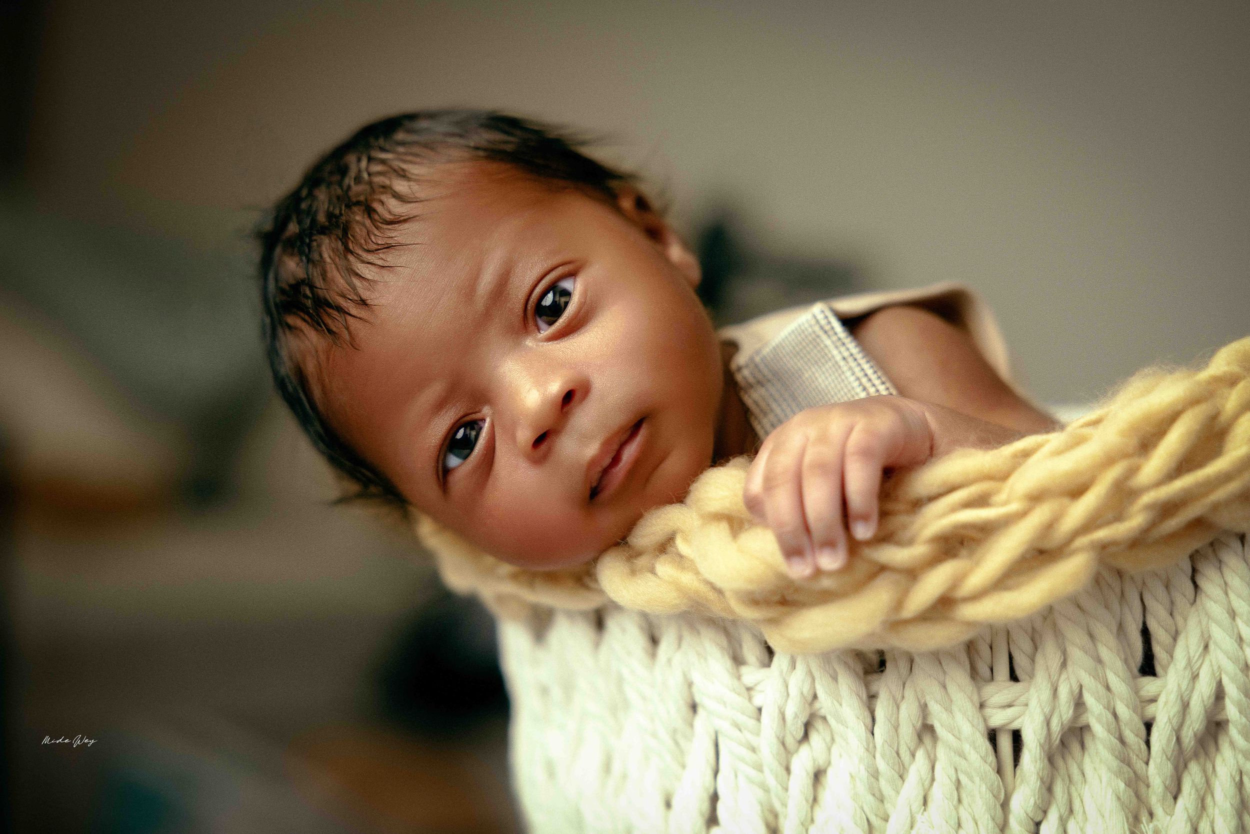 Close-up portrait of baby resting in woven basket with soft yellow blanket.