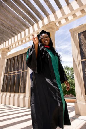 Graduate celebrating in cap and gown under architectural colonnade with dramatic lighting.