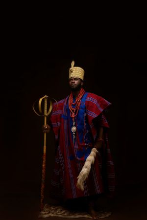 Traditional African royal figure wearing striped ceremonial robes and crown with staff.
