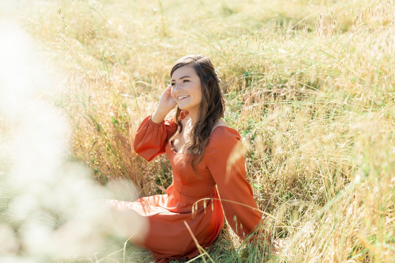 Portrait session in tall grass wearing a burnt orange dress with natural sunlight.