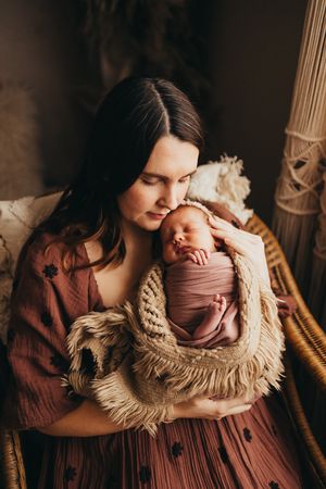 A series of intimate newborn photography shots showing a baby swaddled in mauve fabric against warm brown tones.