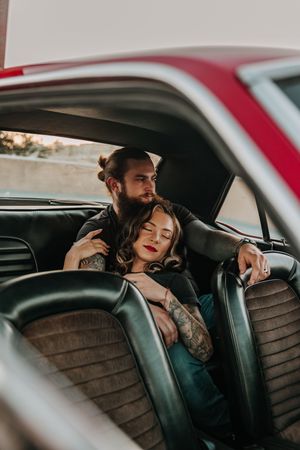 A couple embraces romantically in the backseat of a vintage car with dark leather upholstery.