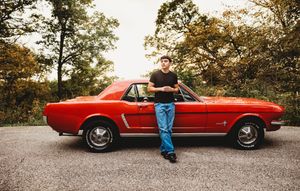 A classic red Mustang convertible parked on a gravel road during sunset with autumn trees in the background.