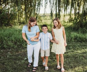 Three people walking together outdoors under willow trees on a sunny day in casual summer attire.