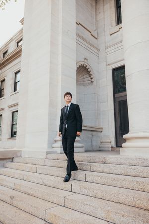 A person in a dark suit descends white marble steps of a grand classical building.