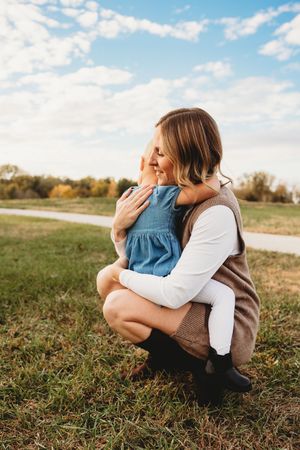 Two people share a tender embrace while sitting together in a grassy field on a sunny autumn day.