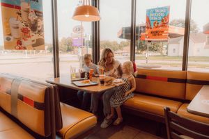 Mother with two young children eating at a retro diner booth by a window in a fast food restaurant.