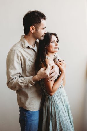 Romantic couple embracing in casual attire against white background.