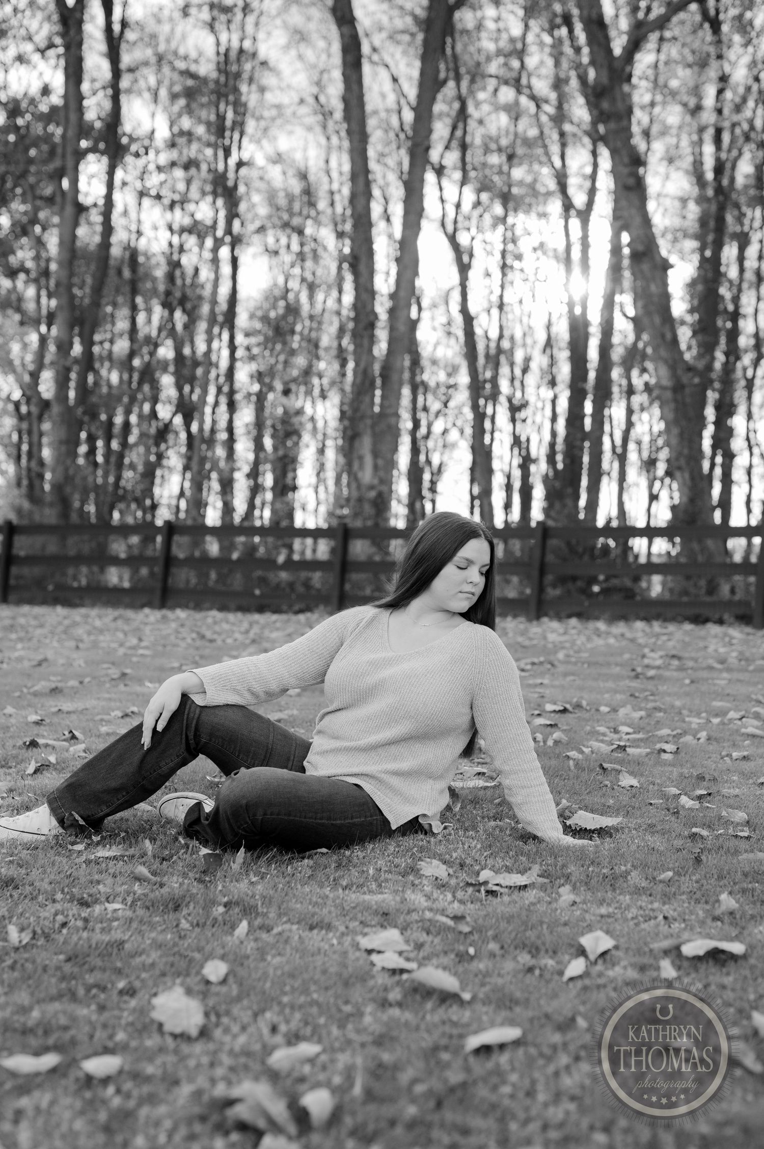 Black and white portrait in a peaceful autumn setting with trees and fallen leaves.