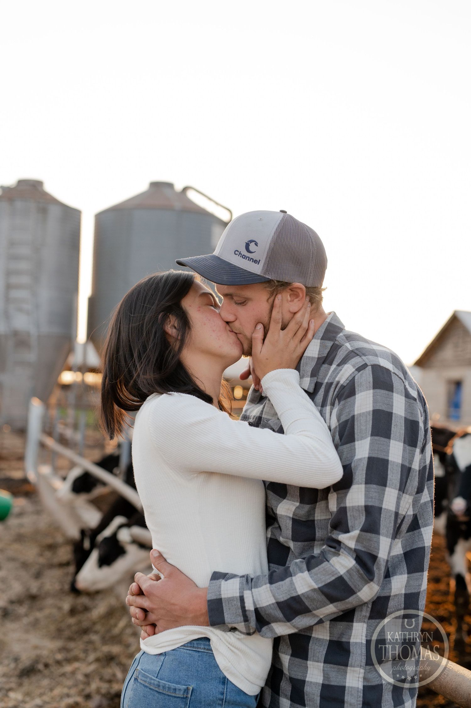 An intimate kiss shared between two people on a dairy farm with silos in the background.