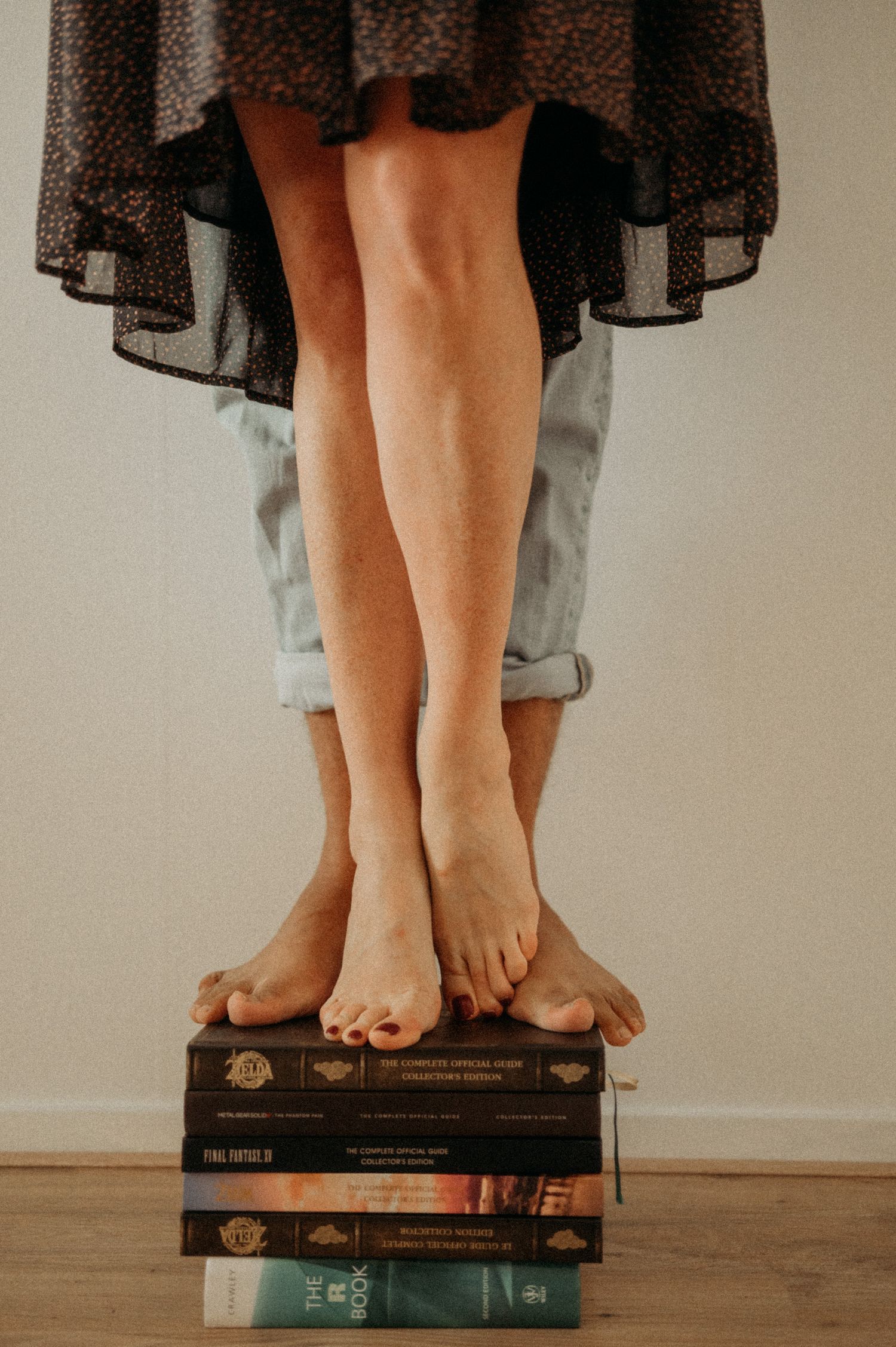 Bare feet standing on stacked vintage books against neutral background.