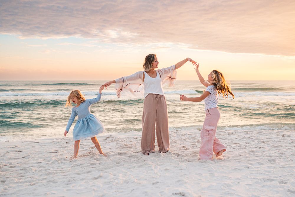 Three figures dancing together on a white sand beach at sunset.